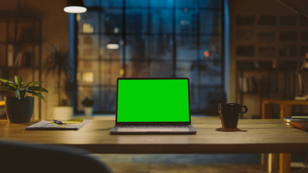 Mock-up Green Screen Laptop Standing on the Desk in the Modern Creative Office. In the Background Warm Evening Lighting and Open Space Studio with City Window View. Mock-up Green Screen Laptop Standing on the Desk in the Modern Creative Office. In the Background Warm Evening Lighting and Open Space Studio with City Window View. chroma key photos stock pictures, royalty-free photos & images
