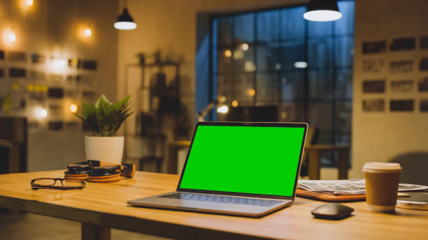 istock Mock-up Green Screen Stanting on the Desktop. In the Background Stylish Modern Office Studio in the Evening with Big Cityscape Window 1269257158