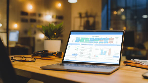 istock Laptop on the Desk in the Office Shows Company Growth Data with Graphs, Charts, Software UI. In the Background Stylish Modern Office Studio in the Evening with Big Cityscape Window 1269257166