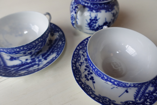 A blue and white Asian-style pottery teapot with a circular opening is in the forefront.  A softly blurred blue English Fine Bone China teacup can be seen through the circular design.