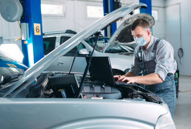 Mechanic in uniform and protective mask work in a car workshop.