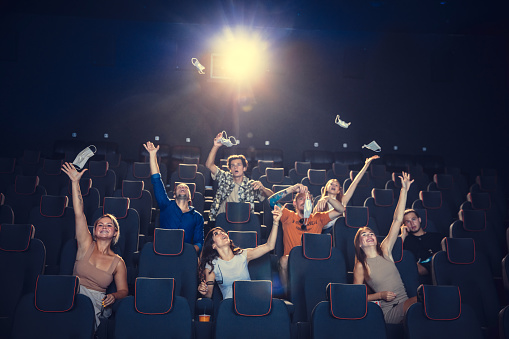 Cinema, movie theatre during quarantine. Coronavirus pandemic safety rules, social distance during movie watching. Men and women wearing protective face mask sitting in a rows of auditorium, eating popcorn.