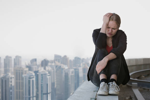 грустная молодая женщина, сидящая на краю высотки с видом на город. рабочий стресс и неудачи. - suicide skyscraper anxiety at the edge of стоковые фото и изображения