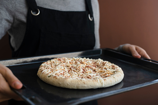 Woman in apron holding oven tray with frozen pizza