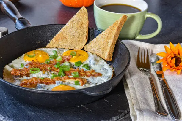 homemade savory breakfast with fried eggs - sunny side up, bacon and toast served in a pan on a dark table - ready to eat food