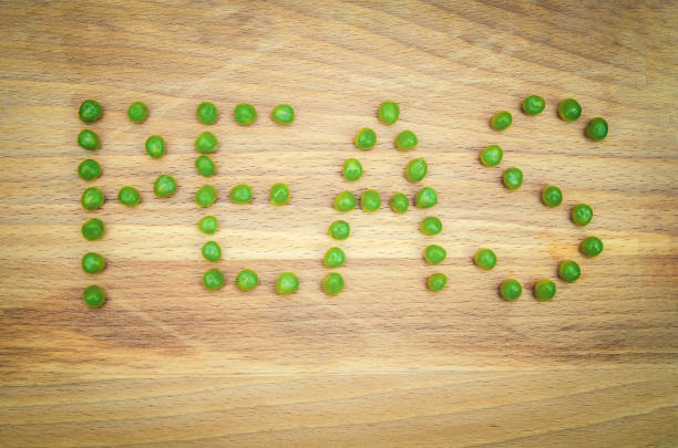 word pea is written in green pea seeds on a wooden background close up