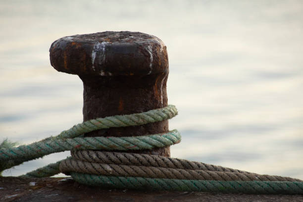 Harbor mooring post at dusk, thick ropes around it,  sea water background. Copy space on the right.