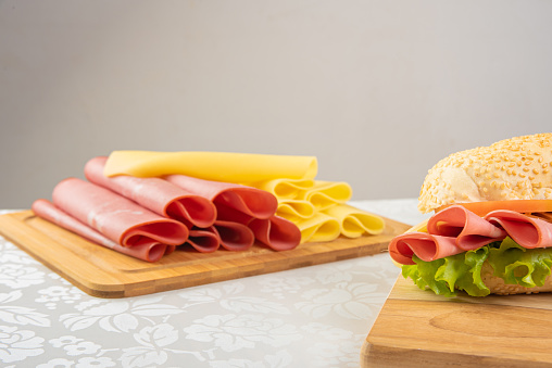 Mortadella sandwich, lettuce, tomato and cheese on a polished board and slices of mortadella and cheese next to it on a cold board on a table with white towel, Selective focus.