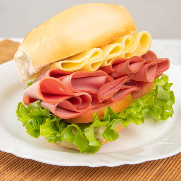 istock Mortadella sandwich, lettuce and cheese on a white plate and a bamboo mat with white background on a table with white towel, Selective focus. 1269277155