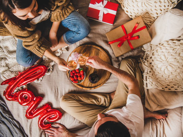 молодая пара сидит в постели, даря подарки пить розовое шампанское - food valentines day color image photography стоковые фото и изображения