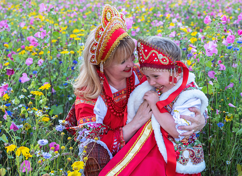 Little preschool girl in wildflower field. Cute happy child in red riding hood dress play outdoor on blossom flowering meadow. Leisure activity in nature with children