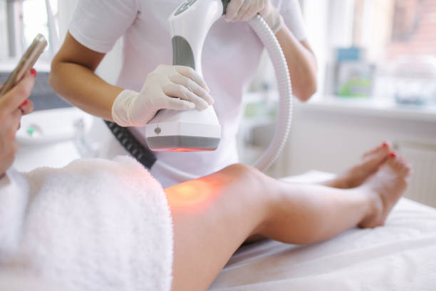 istock Beutiful bussines woman using phone while cosmetologist in white gloves performing radiofrequency lifting procedure on the stomach. Close up 1269285927