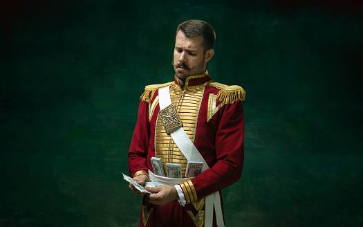 Rich for sale. Young man in suit as Nicholas II isolated on dark green background. Retro style, comparison of eras concept. Beautiful male model like historical character, monarch, old-fashioned.
