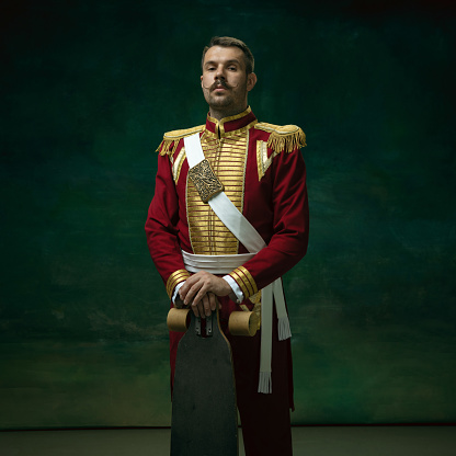 Skater man. Young man in suit as Nicholas II isolated on dark green background. Retro style, comparison of eras concept. Beautiful male model like historical character, monarch, old-fashioned.