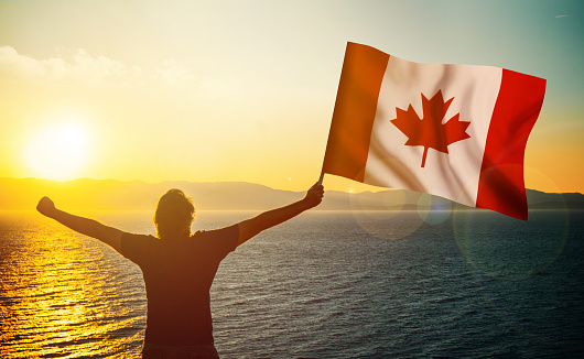 The man is waving the Canadian Flag against the sunrise. Patriotism concept. Horizontal composition with copy space.