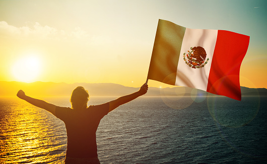 The man is waving the Mexican flag against the sunrise. Patriotism concept. Horizontal composition with copy space.