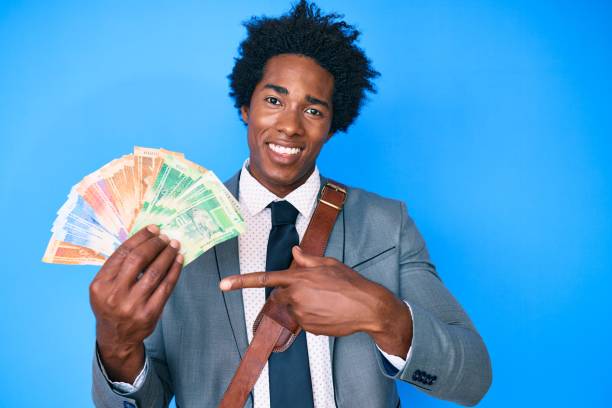 Handsome african american man with afro hair holding south african rand banknotes smiling happy pointing with hand and finger Handsome african american man with afro hair holding south african rand banknotes smiling happy pointing with hand and finger african currency stock pictures, royalty-free photos & images