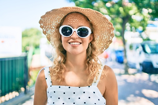 Young beautiful caucasian woman with blond hair smiling happy outdoors on a summer day wearing sunglasses