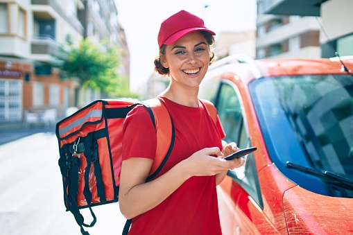 Delivery business worker woman wearing uniform and delivery bag smiling happy using phone