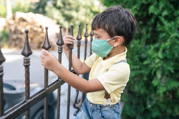 学校のフェンスに立っている保護マスクを持つ小さな男の子 - fence child neighbor peeking ストックフォトと画像