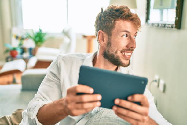 istock Handsome caucasian man smiling happy sitting on the sofa at home using touchpad device 1269303356