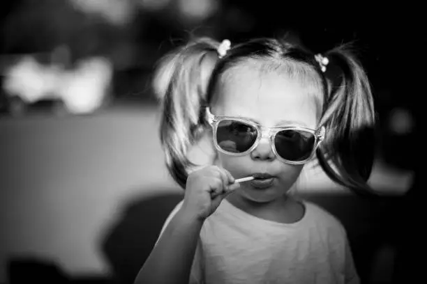 Photo of Black and white portrait of little cute girl in sunglasses with two ponytails.
