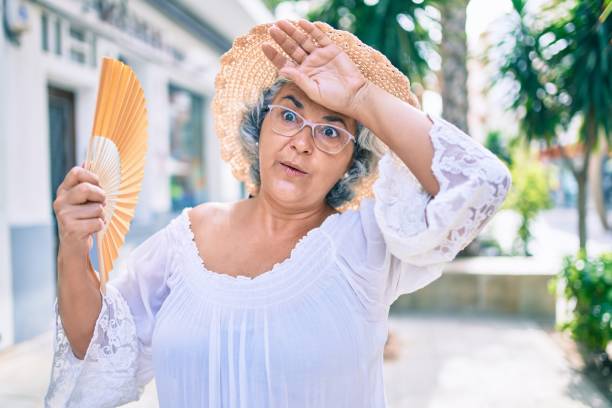 熱波の非常に暑い日にハンドファンを使用して灰色の髪を持つ中年女性 - beautiful senior woman ストックフォトと画像