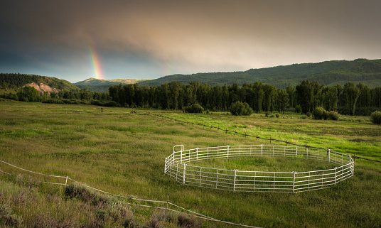 A rainbow is seen in the distant mountains while a horse pen draws your attention to the foreground