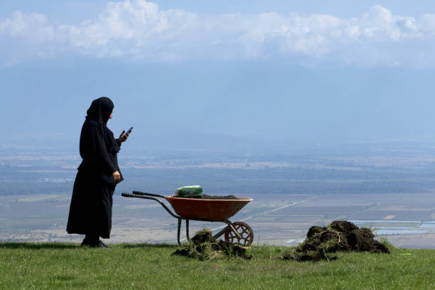 Georgia, Bodbe monastery: old nun during gardening with wheelbarrow on the phone