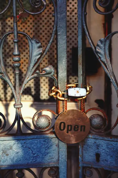 January 28, 2020 - London, UK: Beautiful iron gate with a padlock on a metal chain - closed gates but with funny Open sign - close up, security and protection concept.