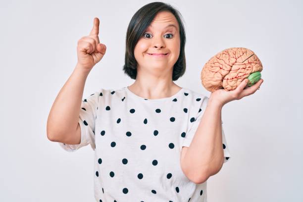 istock Brunette woman with down syndrome holding brain smiling with an idea or question pointing finger with happy face, number one 1269318277