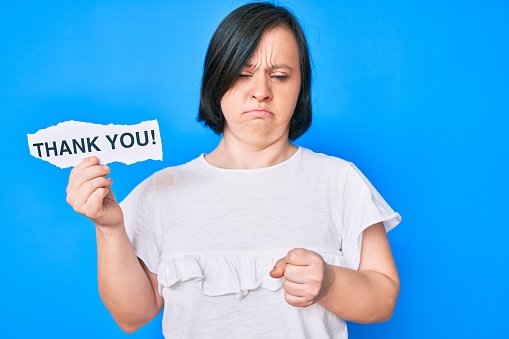 Brunette woman with down syndrome holding thank you paper annoyed and frustrated shouting with anger, yelling crazy with anger and hand raised