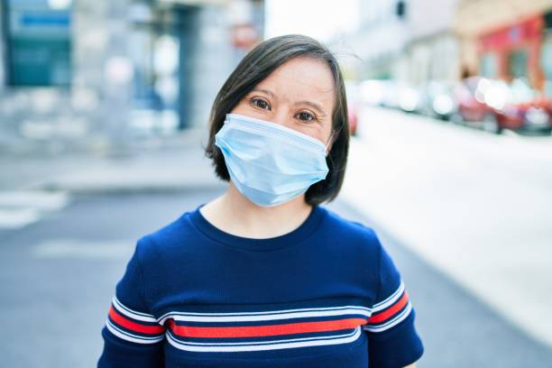 Beautiful brunette woman with down syndrome at the town on a sunny day wearing safety medical mask for coronavirus Beautiful brunette woman with down syndrome at the town on a sunny day wearing safety medical mask for coronavirus town of hope stock pictures, royalty-free photos & images