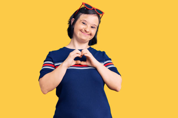 Brunette woman with down syndrome wearing casual clothes smiling in love showing heart symbol and shape with hands. romantic concept. Brunette woman with down syndrome wearing casual clothes smiling in love showing heart symbol and shape with hands. romantic concept. down syndrome stock pictures, royalty-free photos & images