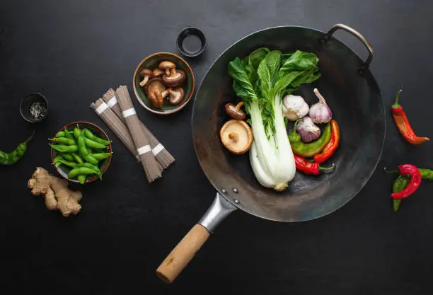 Asian culinary ingredients with wok on a dark surface, Asian food concept, top down view