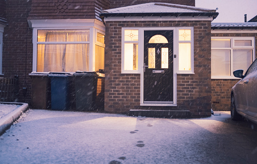 Footprints in the snow are leading away from a home in the evening.