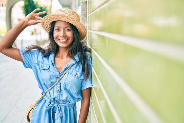 夏の帽子をかぶった若い美しいインドの女性。街で幸せそうに微笑む壁に身を乗り出す。 - women leaning fashion wall ストックフォトと画像