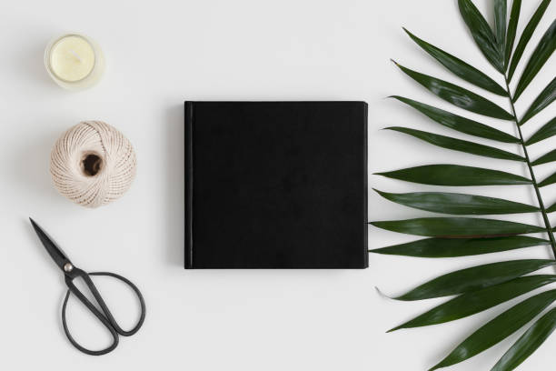 istock Top view of a black book mockup with  workspace accessories and a palm leaf on a white table. 1269325358