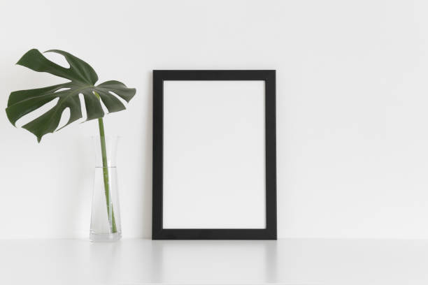istock Black frame mockup with a monstera leaf in a glass vase on a white table. Portrait orientation. 1269325498