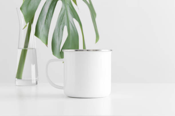 istock Enamel mug mockup with a monstera leaf in a glass vase on a white table. 1269329629