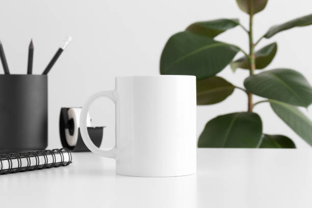 istock White mug mockup with workspace accessories on a white table and a ficus plant. 1269329663