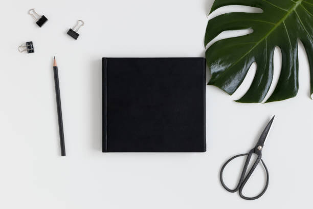 istock Top view of a black book mockup with  workspace accessories and a monstera leaf on a white table. 1269330679
