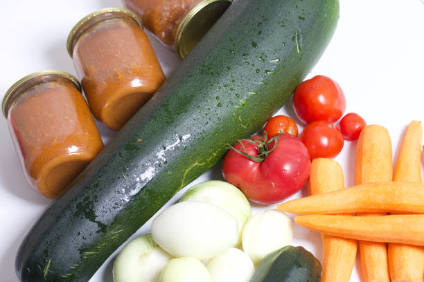 Vegetables for cooking squash caviar. Zucchini, carrots, onions and tomatoes on the table surface. Nearby are jars of squash caviar.