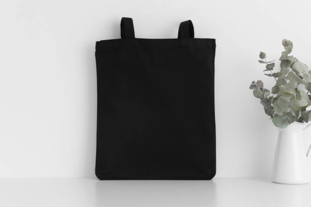 istock Black tote bag mockup with a eucalyptus in a vase on a white table. 1269335756