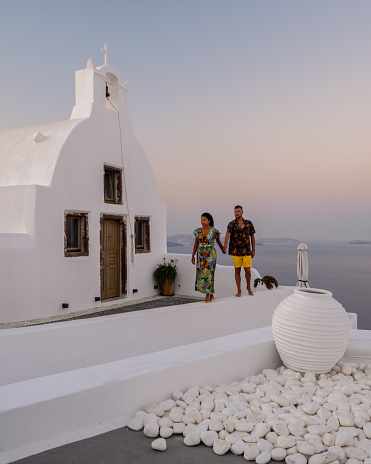 Santorini Greece, young couple on luxury vacation at the Island of Santorini watching sunrise by the blue dome church and whitewashed village of Oia Santorini Greece during sunrise during summer vacation