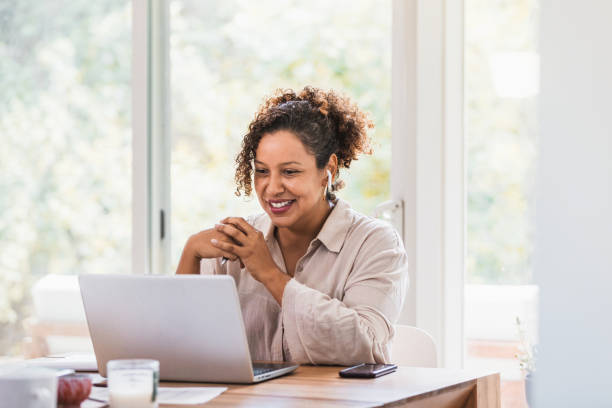 Using laptop and bluetooth earbuds, woman video conferences from home