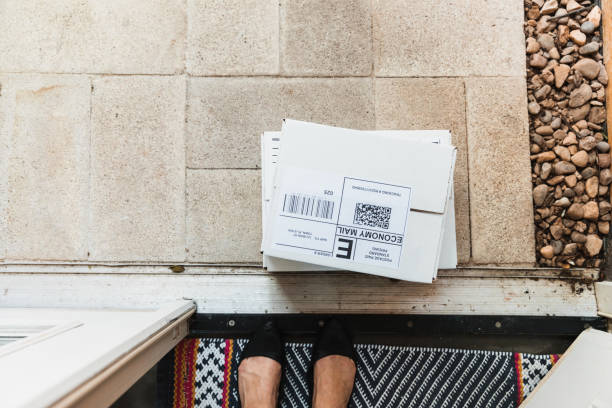 Unrecognizable homeowner looks down at mail left on doorstep The unrecognizable female homeowner looks down at the mail left on her doorstep. bar code photos stock pictures, royalty-free photos & images