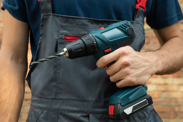 istock Man in overalls holds cordless drill on brick wall background 1269350917