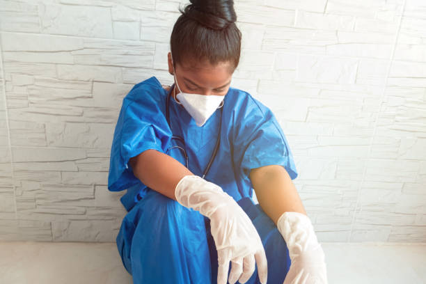 przygnębiona i zmęczona afroamerykańska pielęgniarka nosi maskę i rękawiczki na podłodze szpitala. - hector zdjęcia i obrazy z banku zdjęć