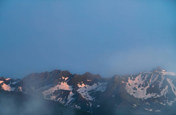 Zell am See tourist resort with sunny Alp mountain summits and white skiing slopes under dramatic cloudy sky